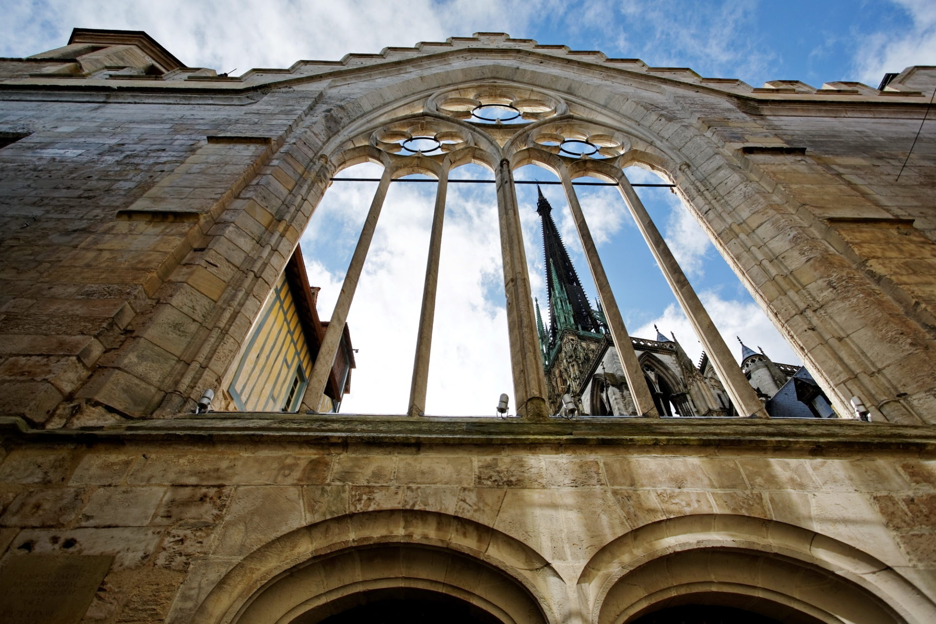 Photo prise de la coure de l Historial Jeanne d Arc en contre plongé avec la nef de la cathédrale apparaissant derrière l'arche de l'historial